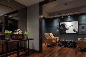 A modern interior with a dark wall, wooden floor, and a large framed artwork. There are two leather armchairs and a small side table.
