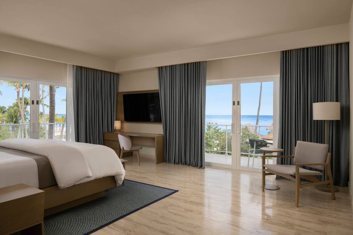 Une chambre d’hôtel avec un lit, un bureau, une chaise, une télévision et une vue sur l’océan.