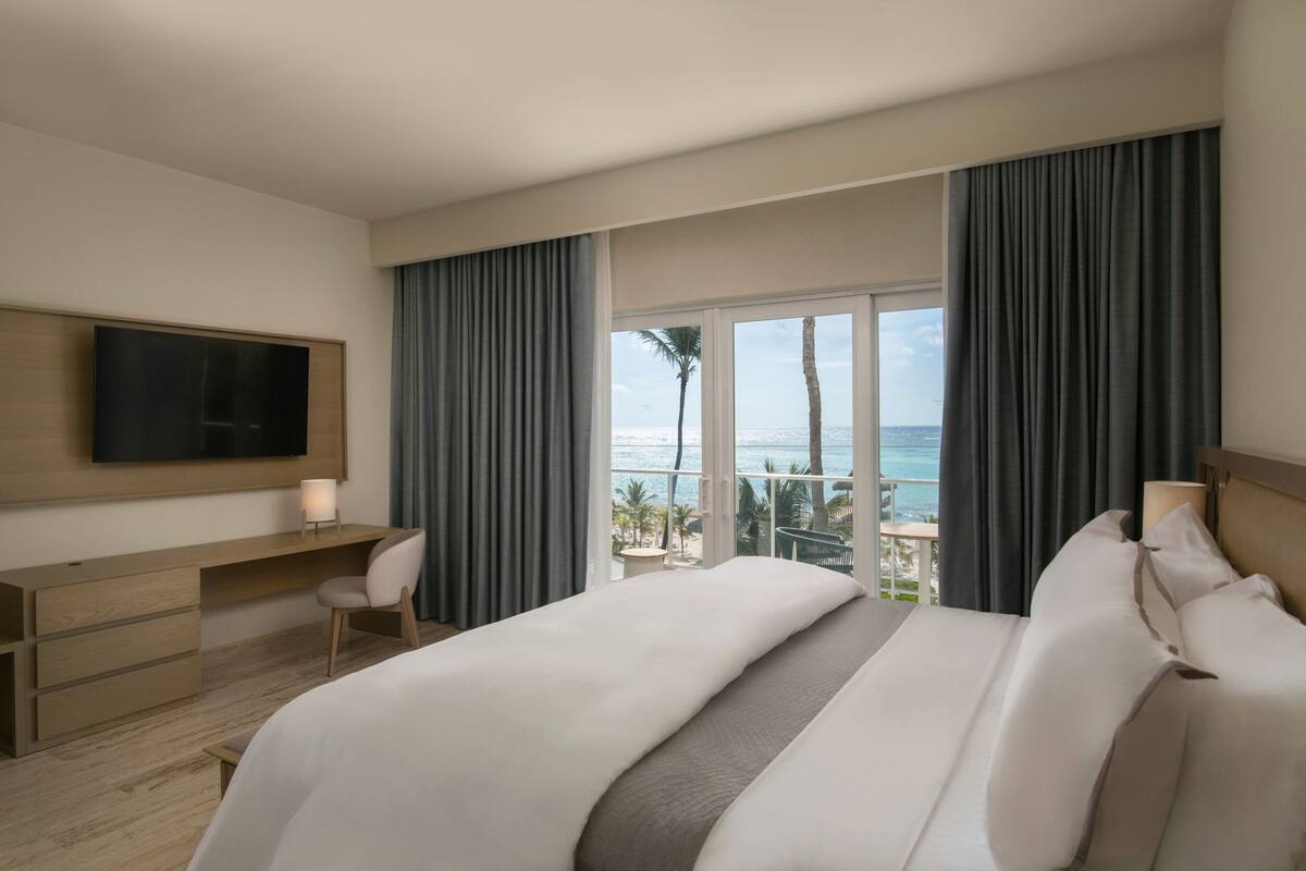 Une chambre d’hôtel comprenant un lit, un bureau, une chaise, une télévision et un balcon avec vue sur l’océan.