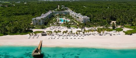 An aerial view of a resort with a central pool, beachfront, and lush greenery.