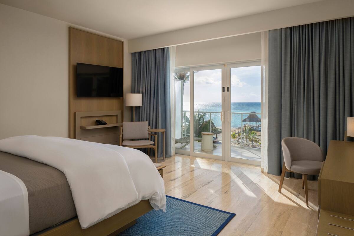 Une chambre d’hôtel comprenant un lit, une télévision, un bureau, une chaise et un balcon avec vue sur l’océan.