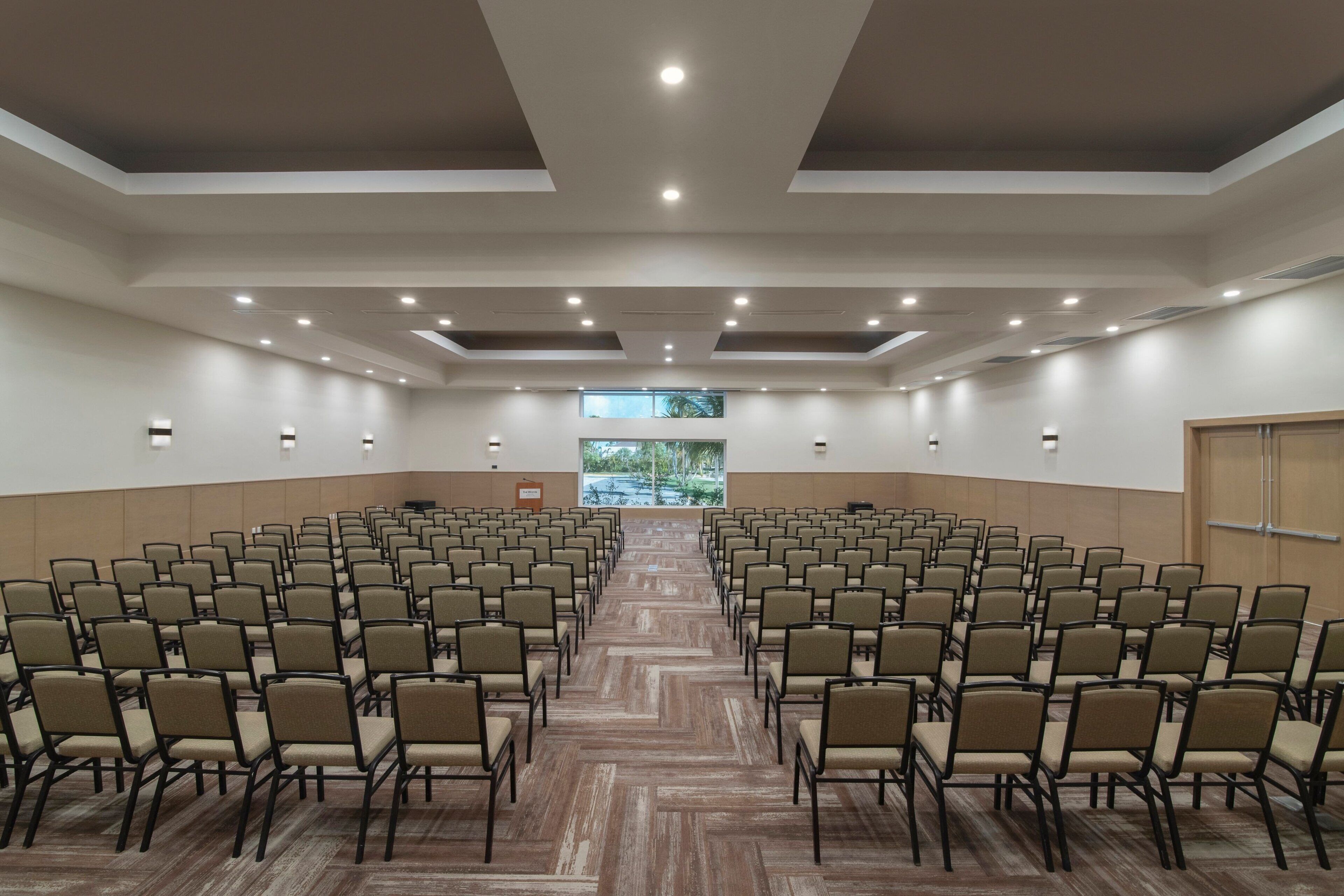 A conference room with rows of chairs, a projector screen, and a large window with a view.
