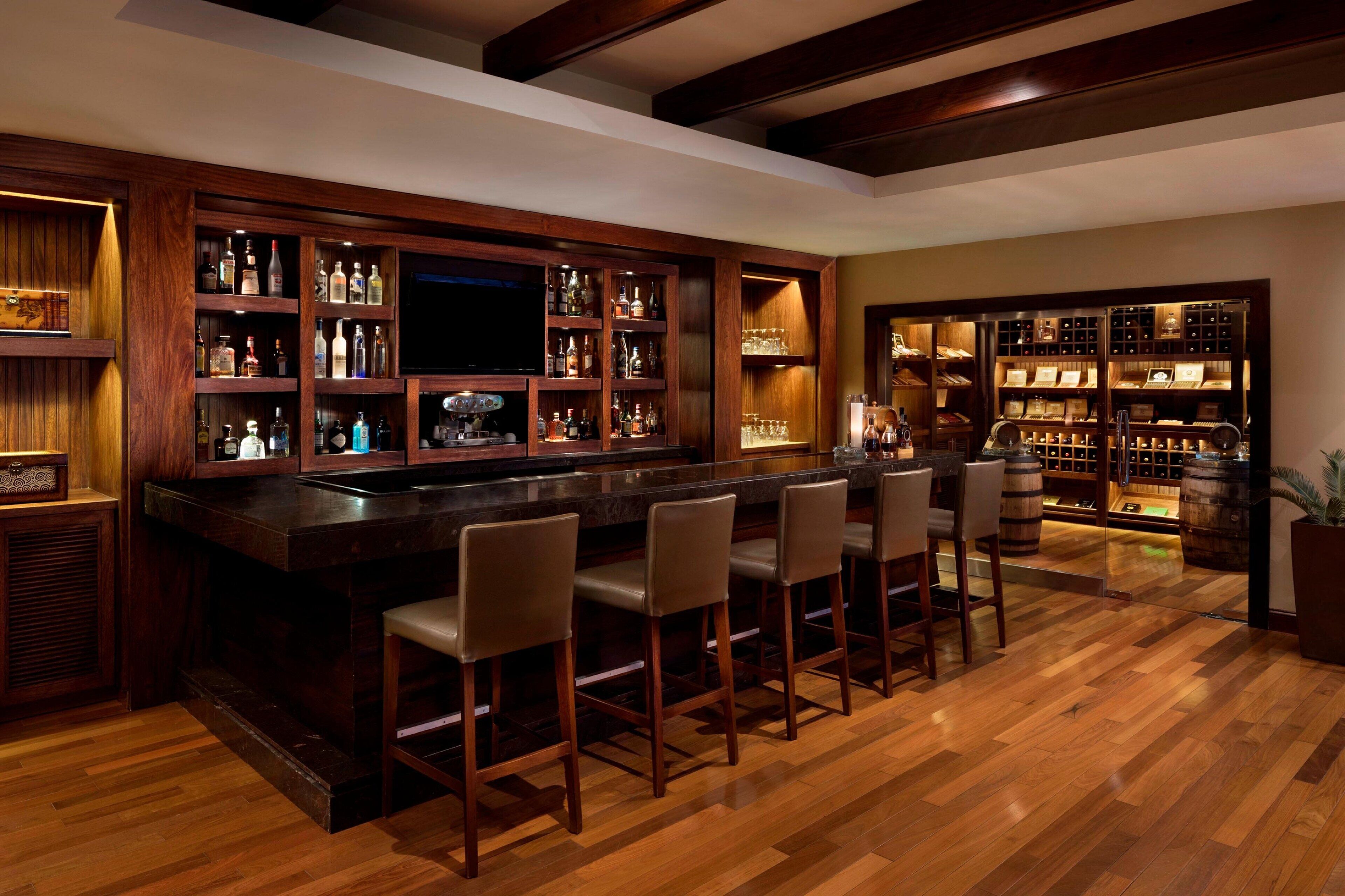 A bar area with wooden shelves, bar stools, and a television.