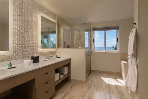 A modern bathroom with a large mirror, a glass-enclosed shower, and a view of the ocean.