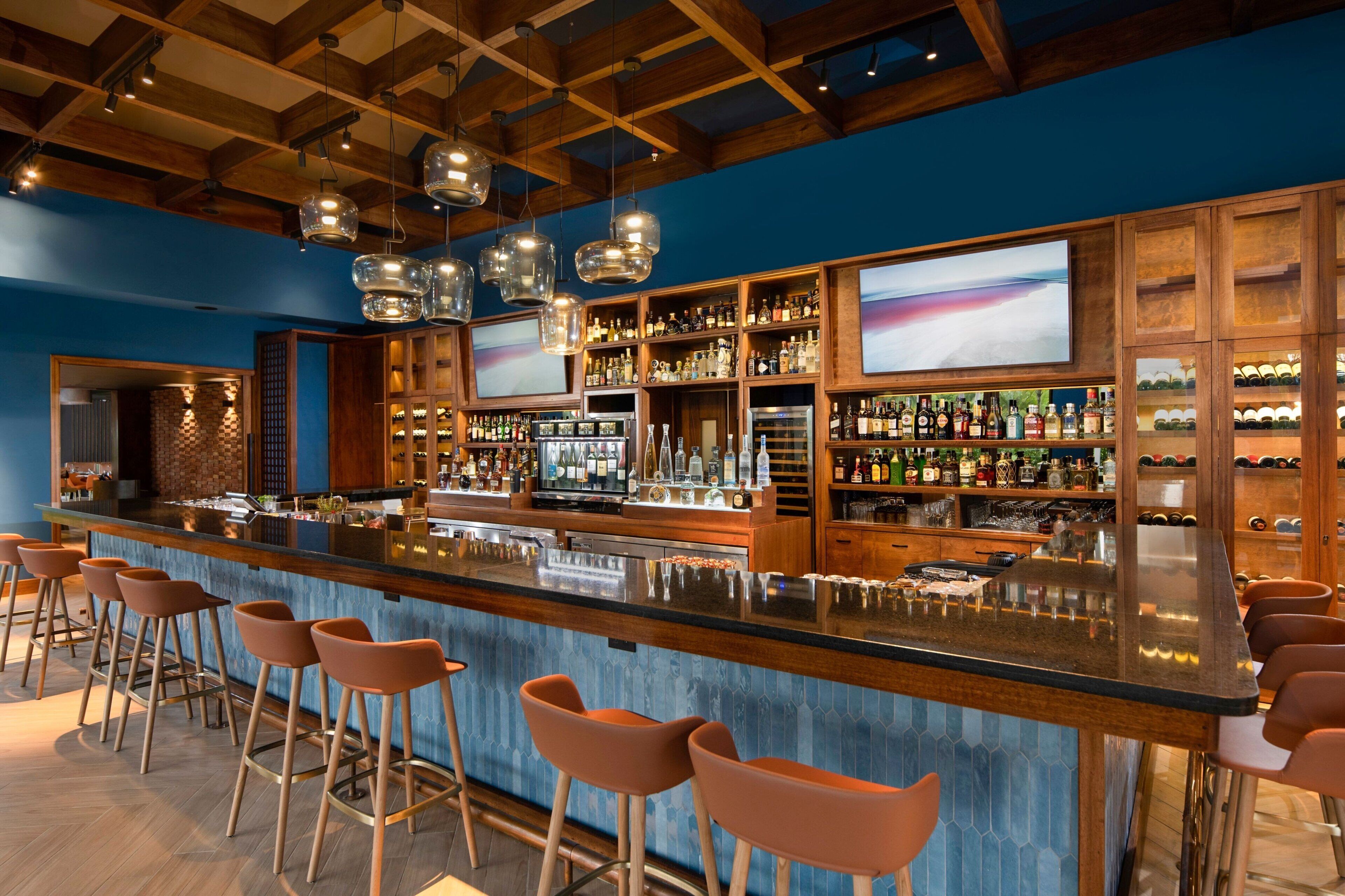 A bar area with a long counter, multiple stools, and shelves stocked with bottles.