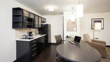 A modern kitchen with a microwave, refrigerator, and coffee maker, a conference table with chairs, and a laptop.