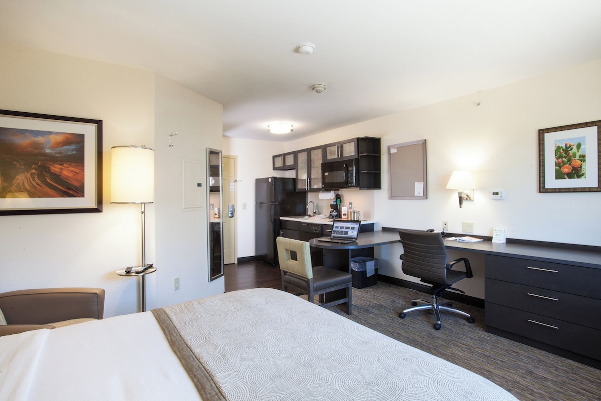 Habitación de hotel con cama, escritorio, kitchenette y una silla.