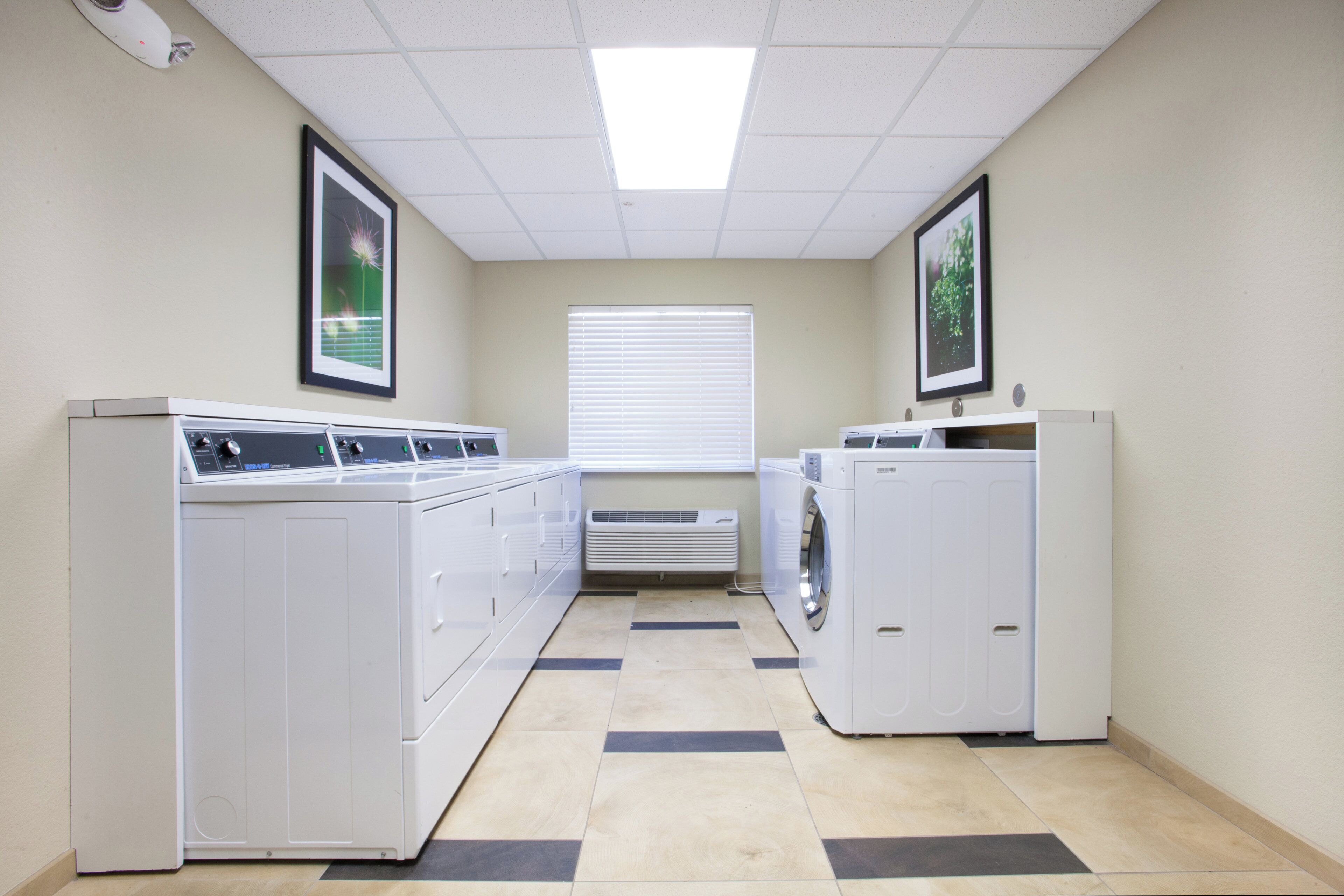 A laundry room with two washing machines and dryers, a vent, and two framed pictures on the walls.