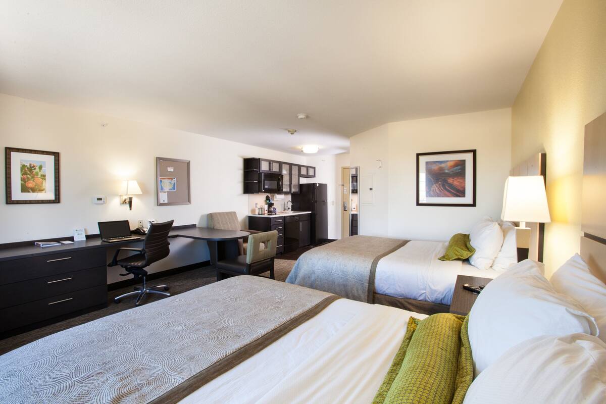 Habitación de hotel con dos camas, un escritorio con computadora, una silla, una lámpara de escritorio y un refrigerador.
