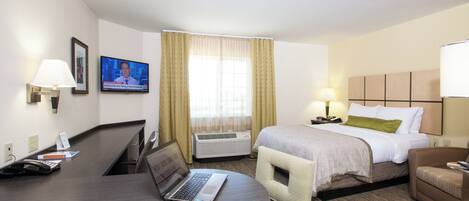 A hotel room with a desk, a bed, a chair, a TV, and an air conditioning unit.