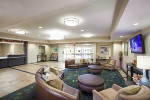 Eine Hotelhalle mit einer Rezeption, einer Sitzecke mit Sofas und Sesseln, einem Fernseher und einem gemusterten Teppich.