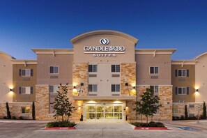 Een hotel met een moderne gevel, een opvallende entree met glazen deuren, en een bordje met de tekst 'CANDLEWOOD SUITES'.