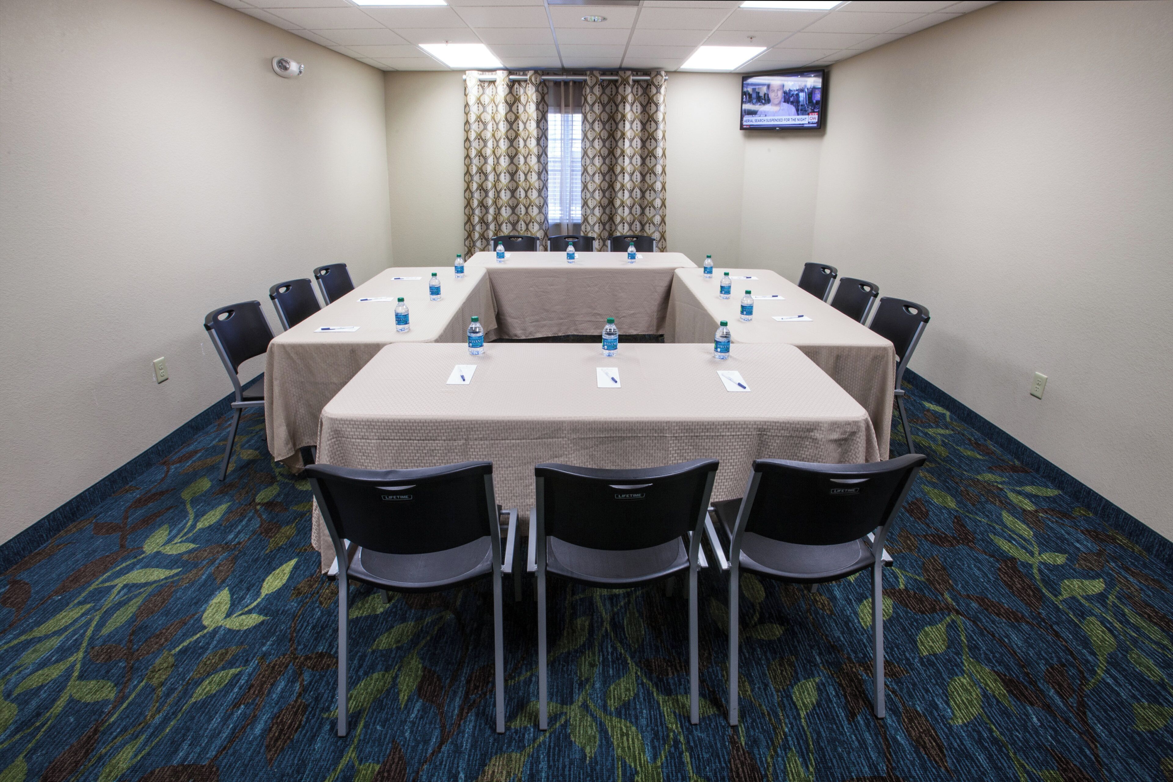 A conference room with a long table, chairs, water bottles, and a television on the wall.