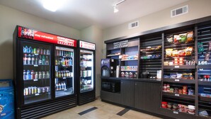 Una estación de bebidas de autoservicio con Coca-Cola y dispensadores de bebidas refrigeradas Candlewood Cupboard, microondas, y una variedad de bocadillos y condimentos.