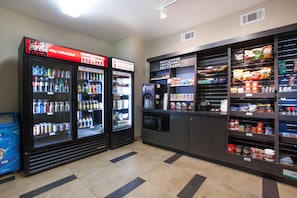 Una estación de bebidas de autoservicio con Coca-Cola y dispensadores de bebidas refrigeradas Candlewood Cupboard, microondas, y una variedad de bocadillos y condimentos.