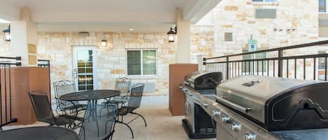 An outdoor patio with a barbecue grill, metal chairs, and a stone wall.