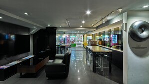 Un moderno vestíbulo de hotel con zona de bar, asientos, máquinas expendedoras y un reloj de pared grande.