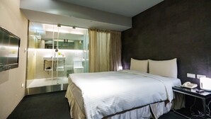 Una habitación de hotel con cama, mesita de noche y baño visible a través de un mamparo de vidrio.