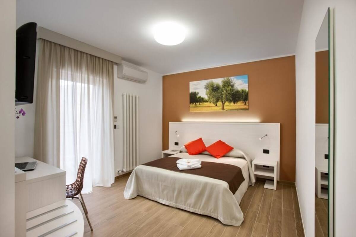 Ein Hotelzimmer mit Bett, Schreibtisch, Stuhl, einem Bild an der Wand und einem Fenster mit Vorhängen.
