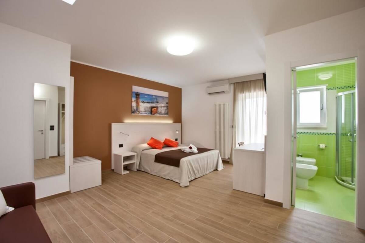 Ein modernes Hotelzimmer mit Bett, Nachttisch und einem Badezimmer mit Dusche und Toilette.