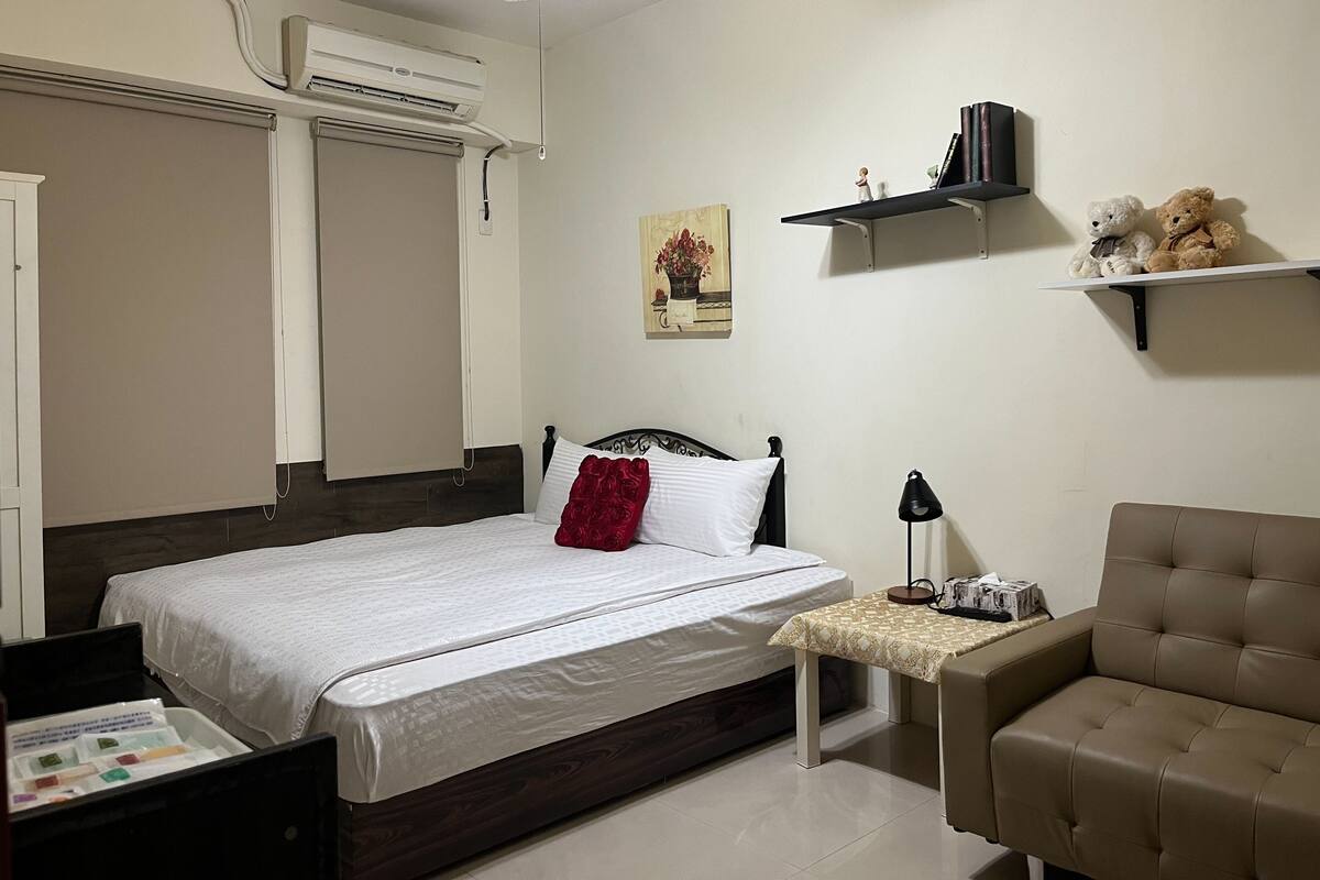 A bedroom with a bed, bedside table, lamp, and a chair.