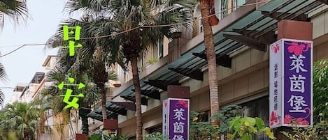 A street view with palm trees and potted plants. There are banners with Chinese characters on a building.