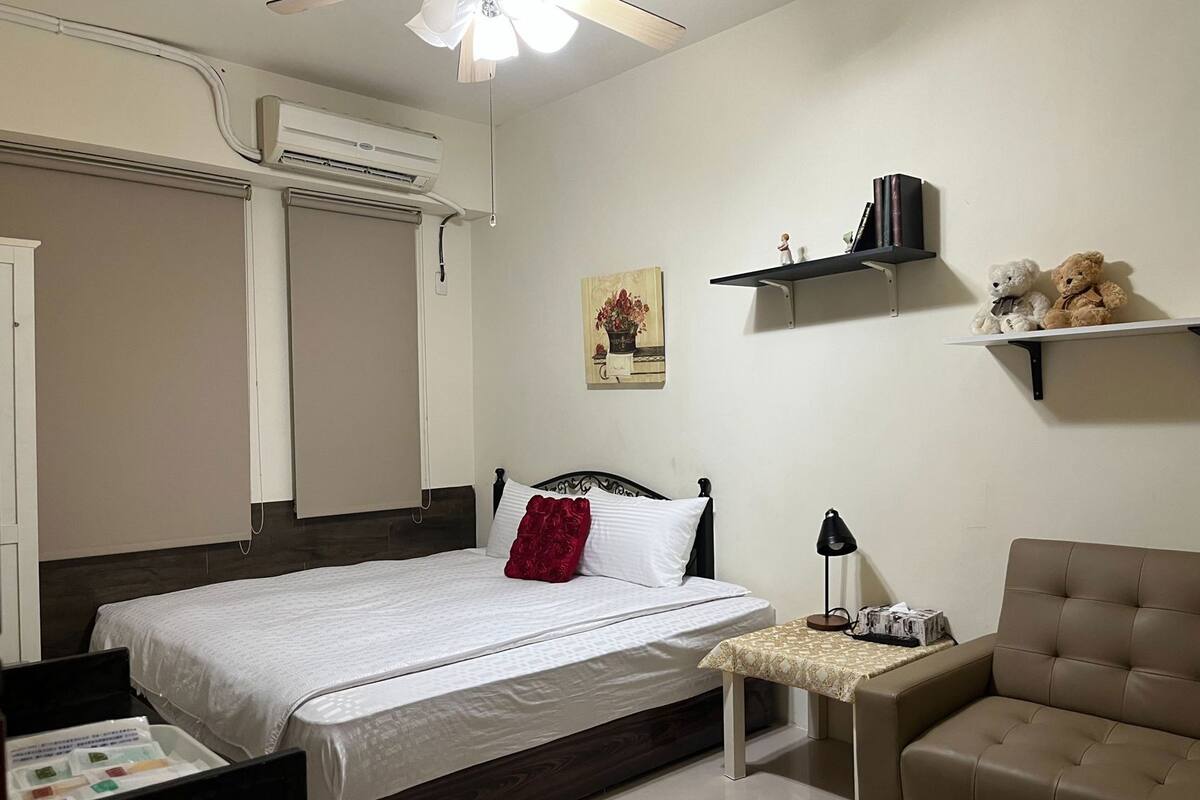 A bedroom with a bed, bedside table, lamp, and a sofa.