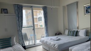 A hotel room with a large bed, a smaller bed, a wardrobe, a desk, and a balcony with a view of the building.