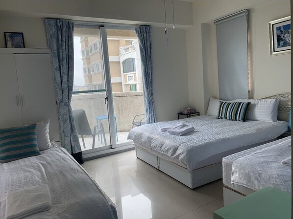 A hotel room with a large bed, a smaller bed, a wardrobe, a desk, and a balcony with a view of the building. - Rhine Castle Hotel (Taichung)