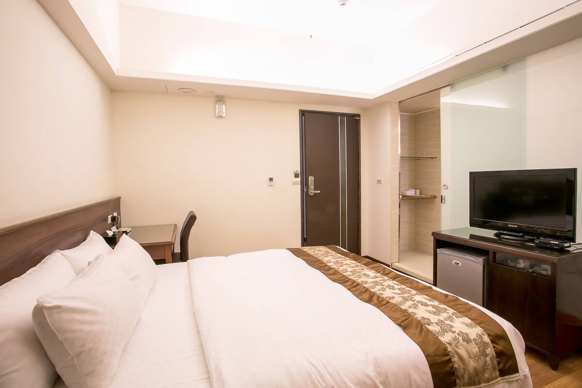 A hotel room with a bed, a television, a desk, and a wardrobe.