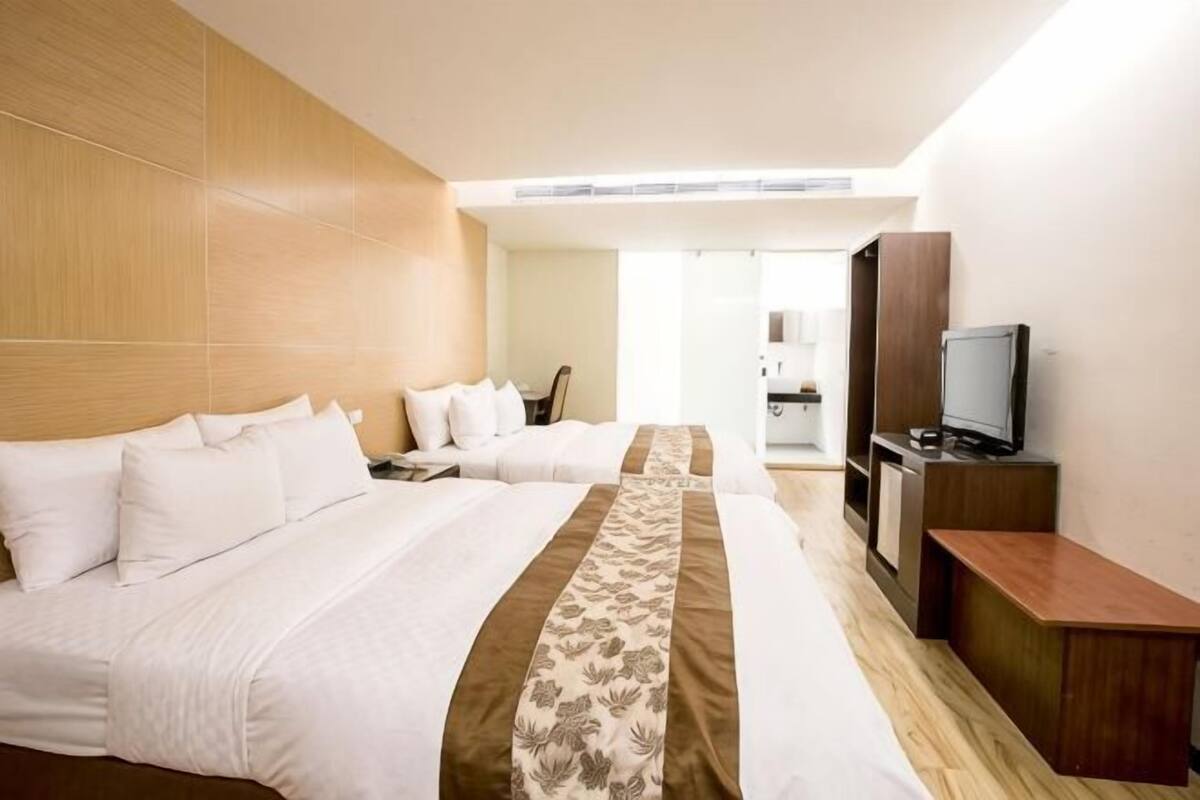 A hotel room with two beds, a TV, and a wooden headboard.