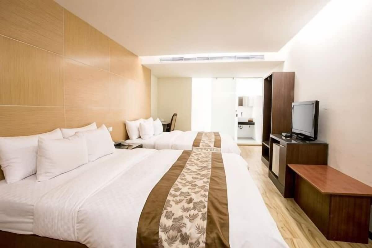 A hotel room with two beds, a TV, and a wooden headboard.