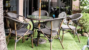 Un patio con sillas de mimbre, una mesa redonda y una sombrilla verde.