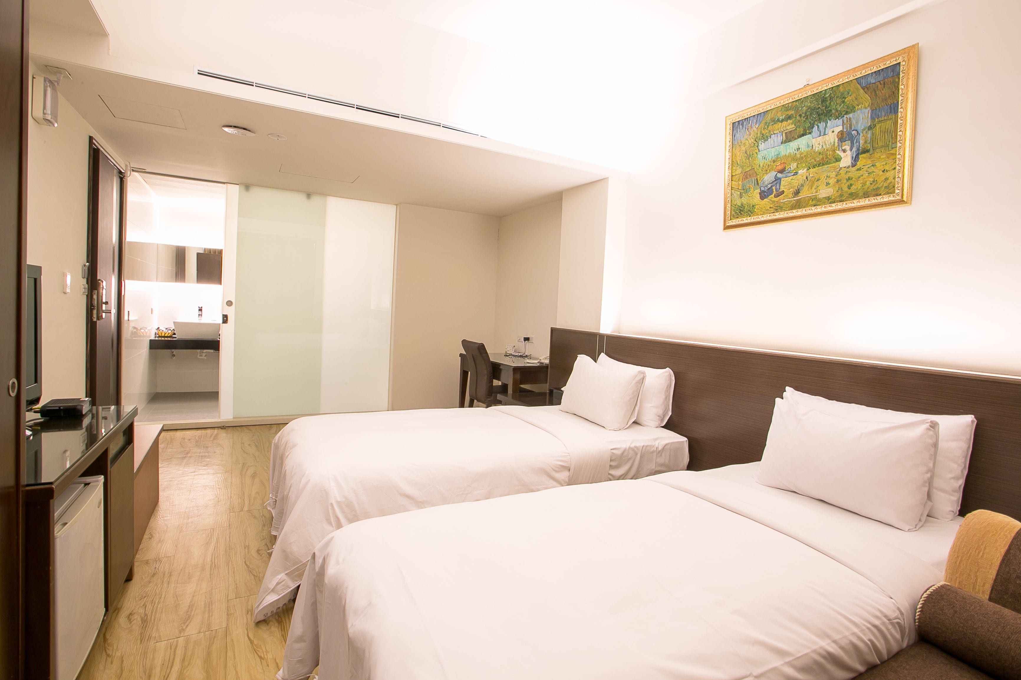 A hotel room with two beds, a desk, a chair, and a painting on the wall.