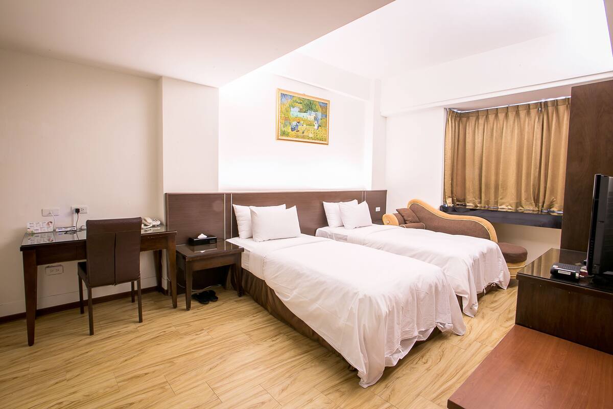 A hotel room with two beds, a desk with a chair, a TV, and a painting on the wall.