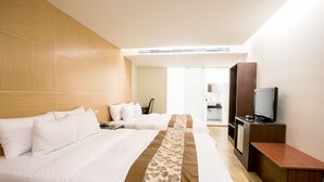 Habitación de hotel con dos camas, televisión, escritorio y baño visible a través de una puerta abierta.