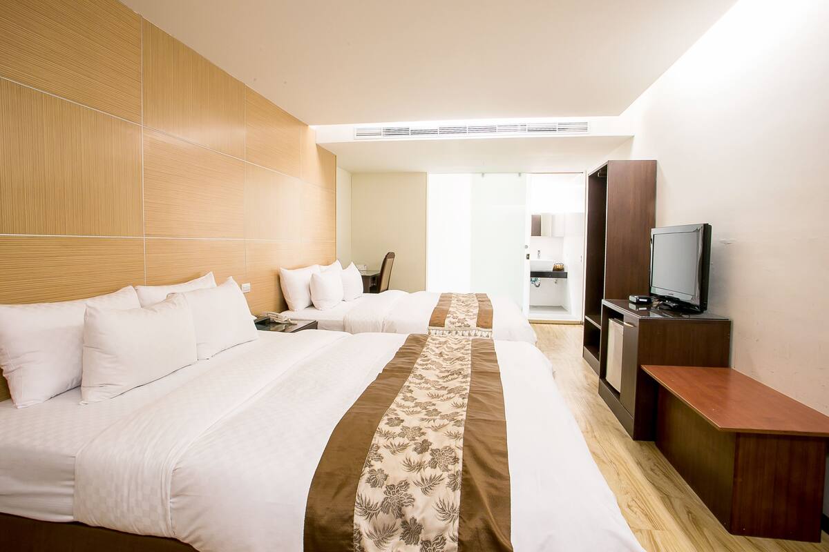 A hotel room with two beds, a TV, a desk, and a bathroom visible through an open door.