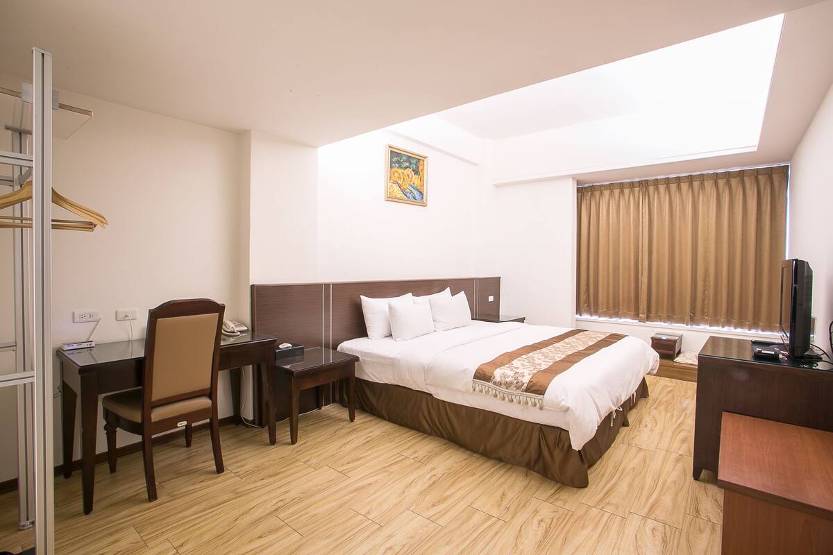 A hotel room with a bed, desk, chair, and a television.