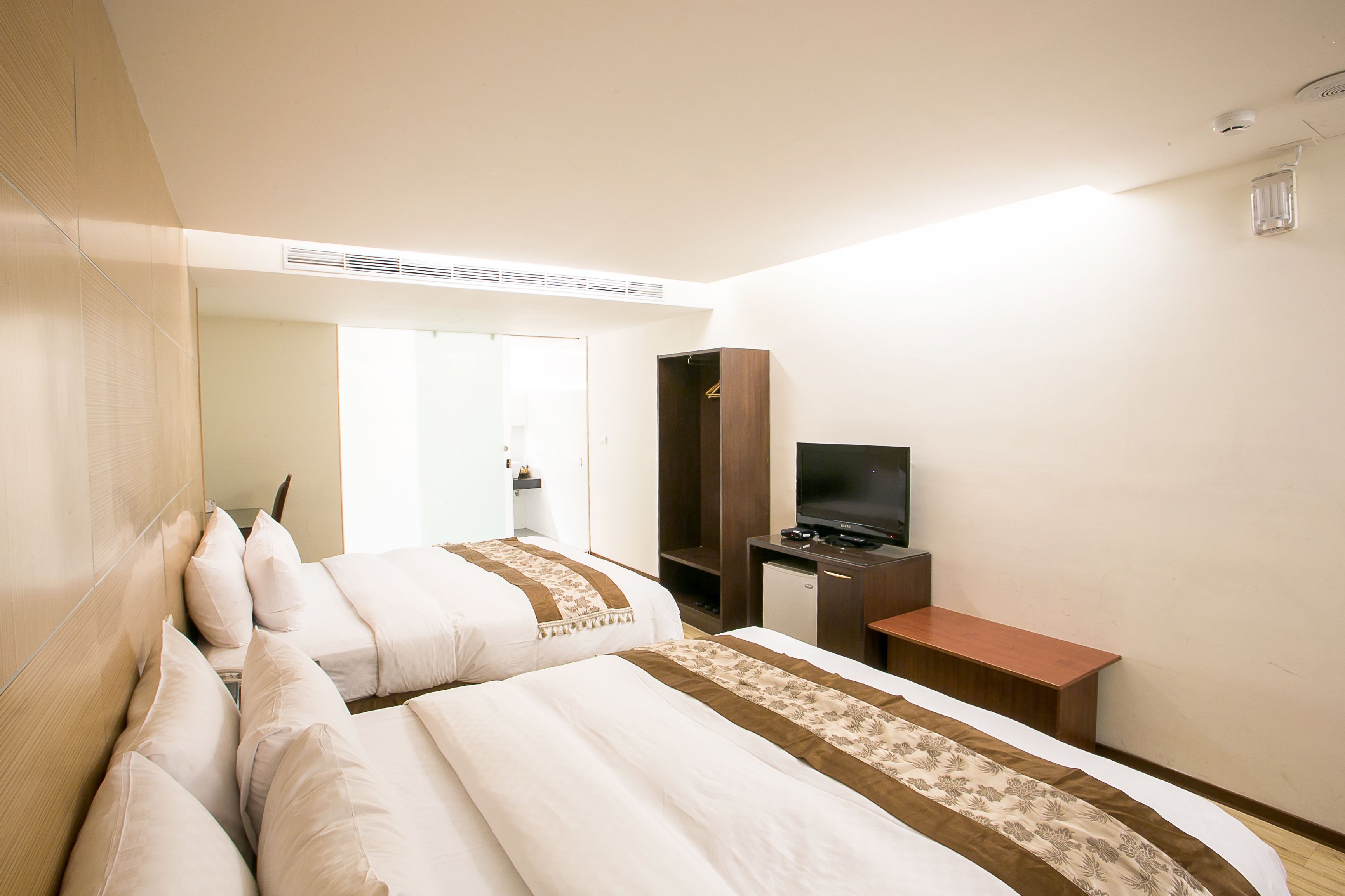 A hotel room with two beds, a TV, a desk, and a wardrobe.