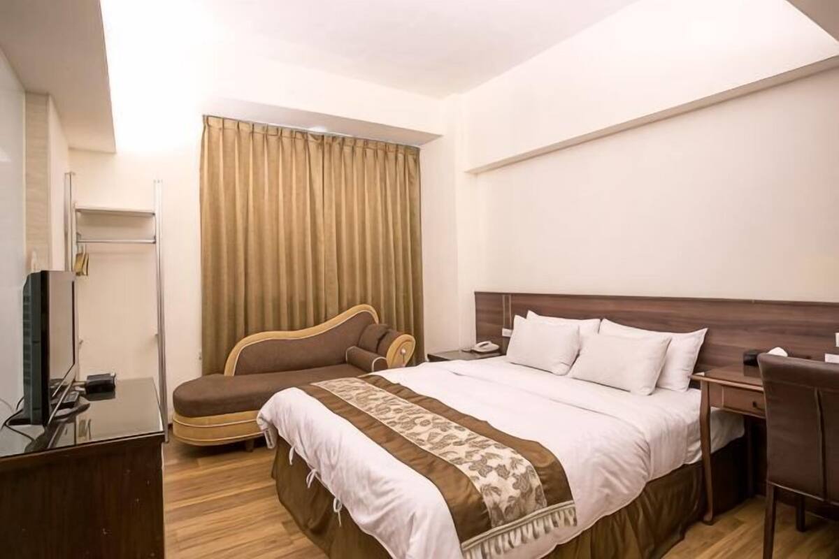 A hotel room with a bed, a desk, a chair, a television, and a curtain.