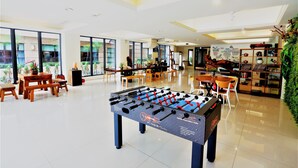 Amplio espacio interior con mesa de fútbol, mesas de madera, sillas y un ventanal que ofrece vistas al exterior.