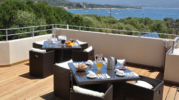 A terrace with wicker furniture, a table set with breakfast items, and a scenic view of the sea and mountains. - Casa Murina Hôtel Demeure Ecologique (Serra-di-Ferro)