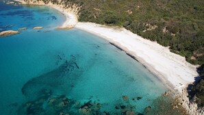An aerial view of a coastal area with clear turquoise waters, a sandy beach, and dense vegetation on the hillside. - Casa Murina Hôtel Demeure Ecologique (Serra-di-Ferro)