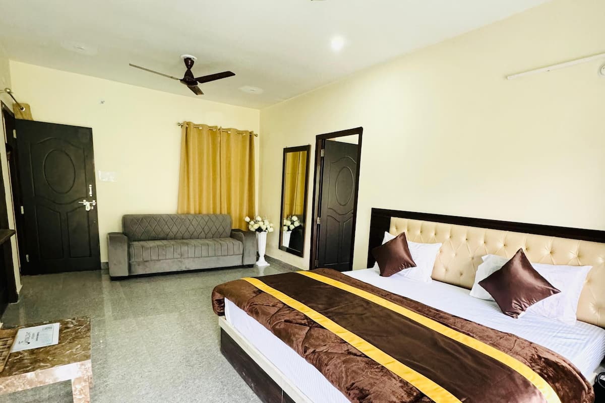 A hotel room with a large bed, a sofa, a ceiling fan, and a door.