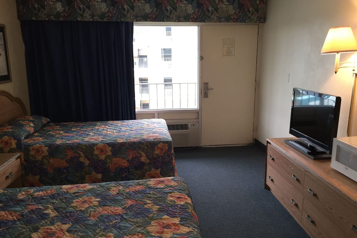 A hotel room with two beds, a television, a dresser, and a window with curtains.