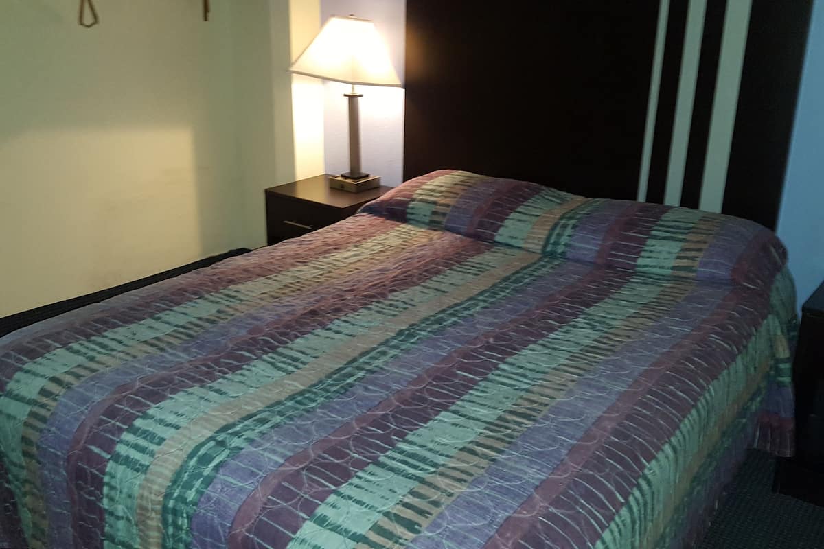 A bed with a multicolored quilt, a bedside lamp, and a dark headboard.