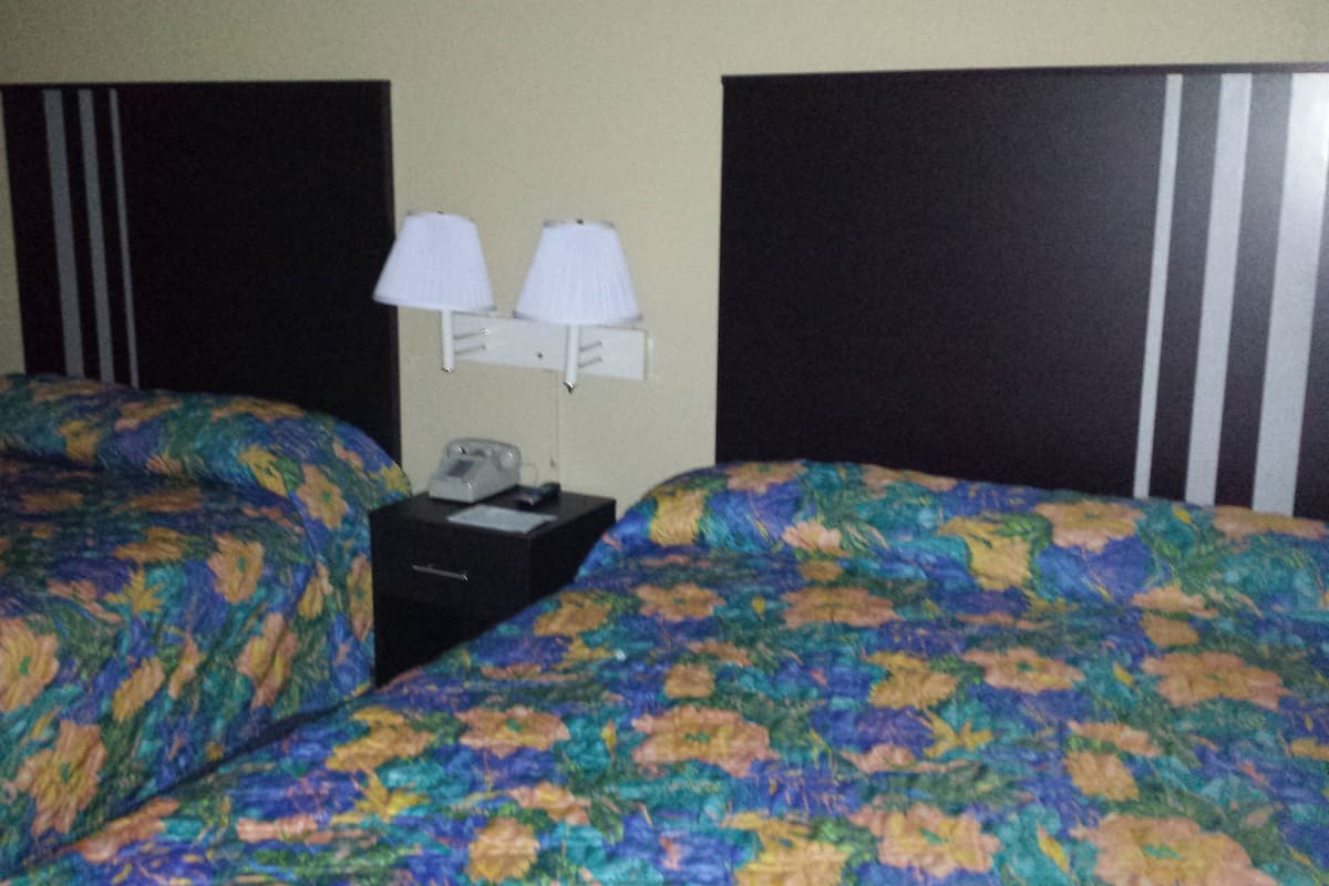 A hotel room with two beds, each with a floral-patterned bedspread. There are two bedside tables with lamps and a telephone on one of them.