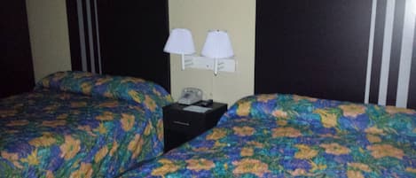 A hotel room with two beds, each with a floral-patterned bedspread. There are two bedside tables with lamps and a telephone on one of them.