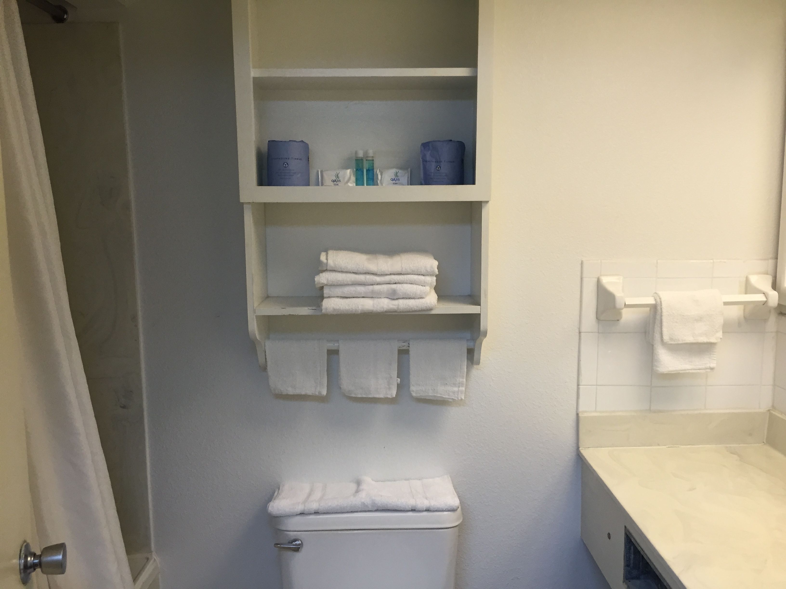 Un baño con inodoro, lavamanos y un estante con toallas y artículos de aseo.
