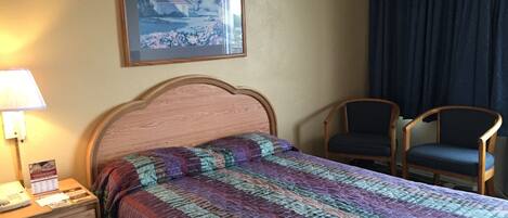 A hotel room with a bed, a nightstand with a lamp, two chairs, and a framed picture on the wall.